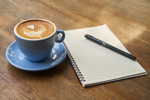 notepad with a pen on top next to a cup of coffee